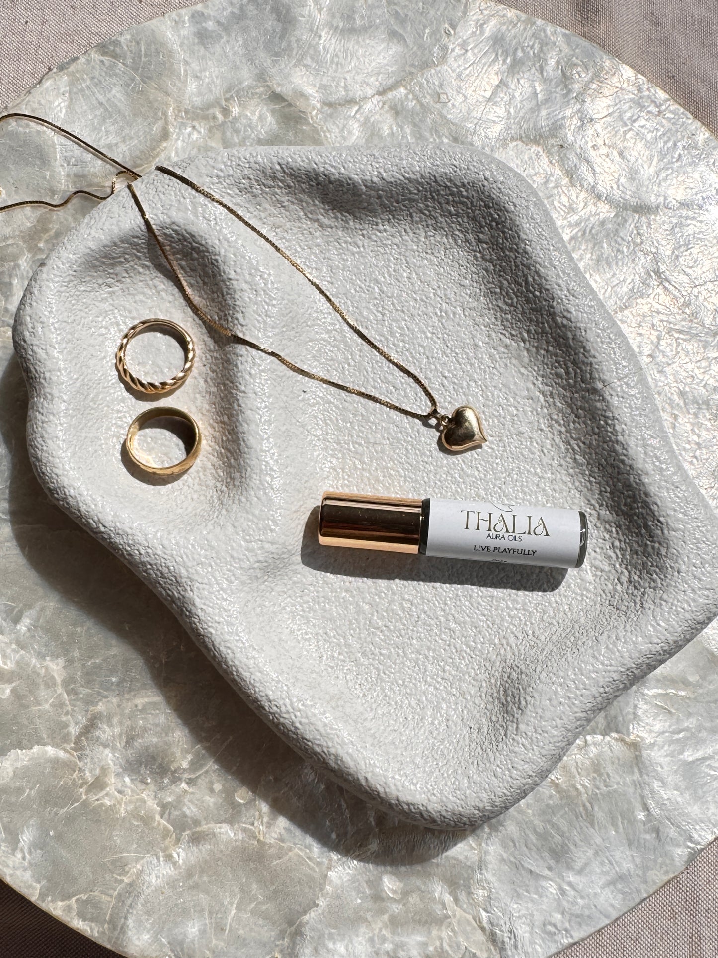 Roll-on bottle Thalia aura oil and jewelry on a textured stone surface