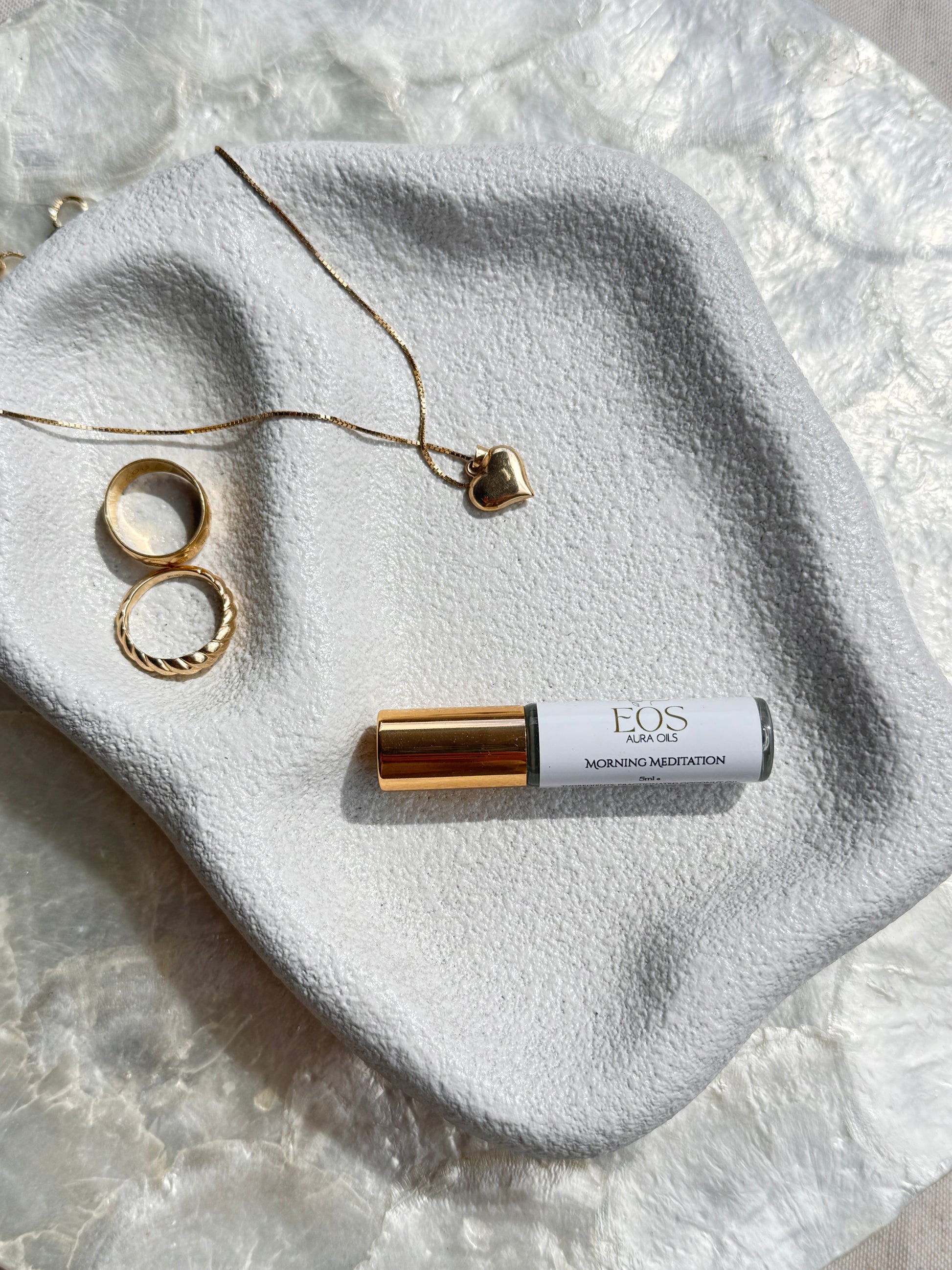 Roll-on bottle Eos aura oil and jewelry on a textured stone surface