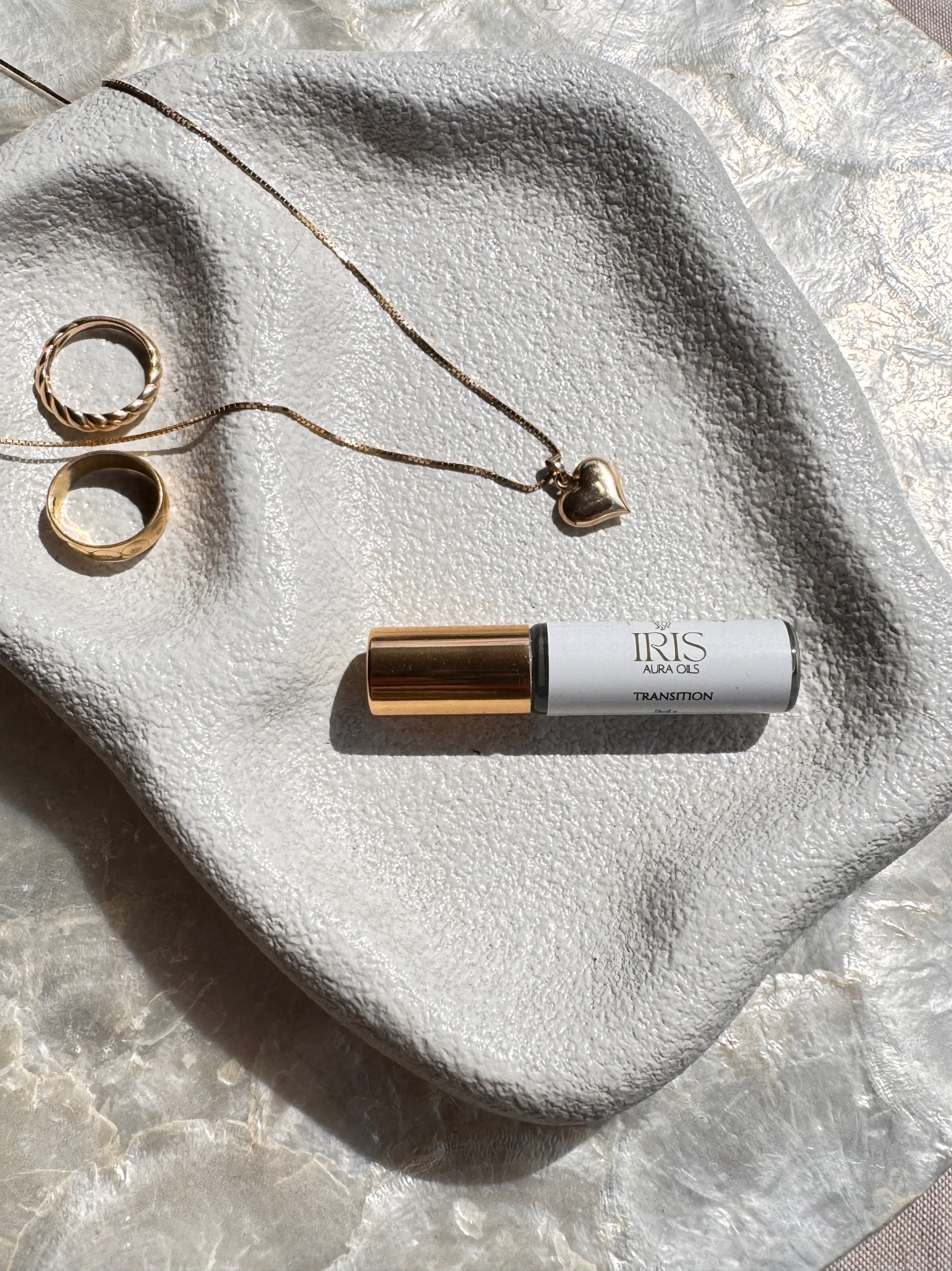 Roll-on bottle iris aura oil and jewelry on a textured stone surface